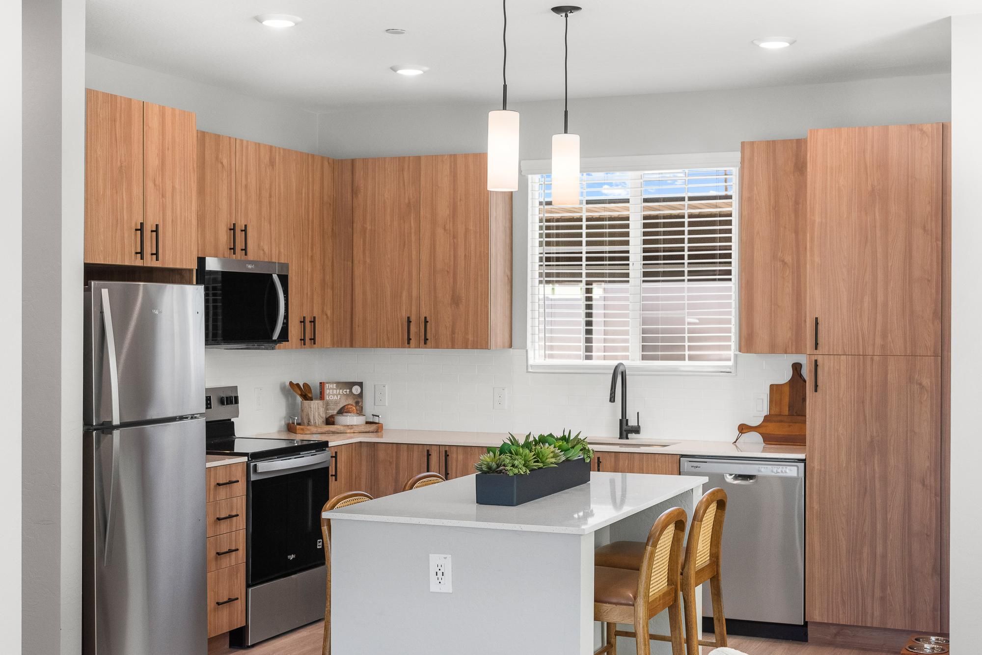 Modern kitchen with wood cabinets, stainless steel appliances, island with stools, and hanging lights.