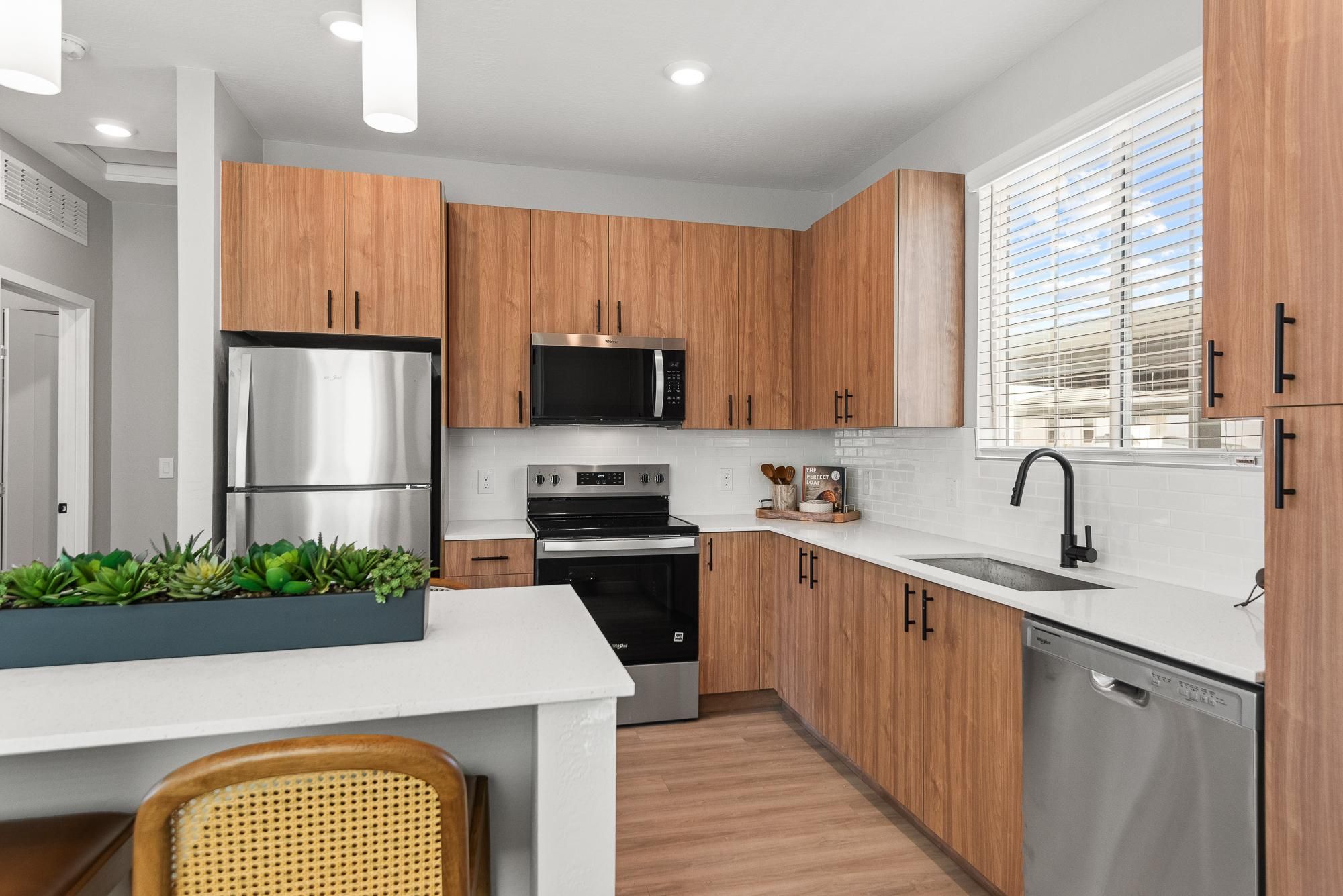 Verge Apache Junction modern kitchen with wood cabinets, stainless steel appliances, white countertops, and a potted plant on the island.