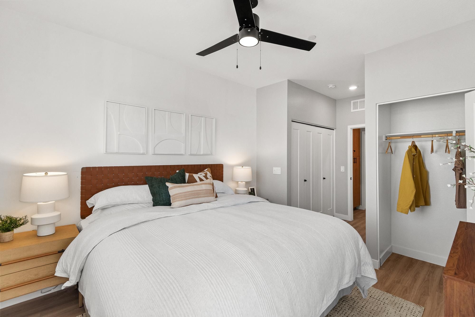 Modern bedroom with a large bed, neutral bedding, nightstands, and open closet with yellow coat hanging.