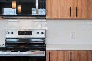 Modern kitchen with wooden cabinets, white tile backsplash, and stainless steel stove under a black microwave.