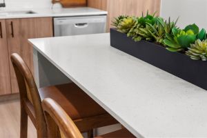 Modern kitchen with a white countertop, wooden chairs, and a planter box of succulents as decoration.